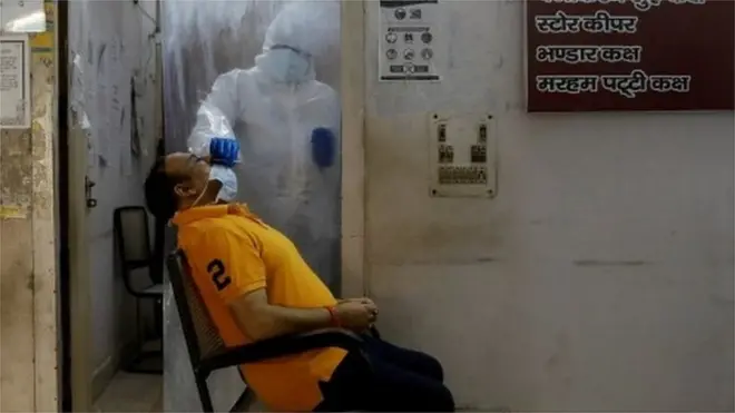 A health worker in personal protective equipment collects a sample using a swab from a girl at a health centre to conduct tests in Delhi, 27 June