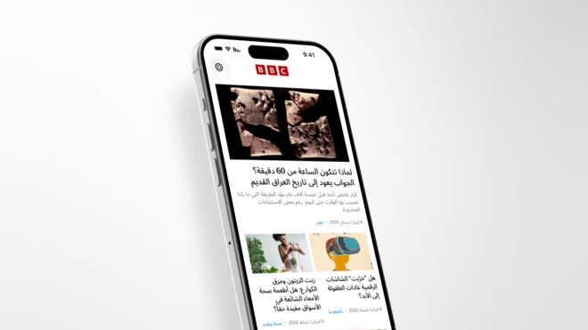 صورة لهاتف آيفون تظهر على شاشته نسخة من تطبيق بي بي سي نيوز عربي. يعرض التطبيق قسماً من القصص المختارة، أعلاها وأبرزها قصة عنوانها "لماذا تتكون الساعة من 60 دقيقة؟ الجواب يعود إلى تاريخ العراق القديم" مع صورة للوح سومري يرجع تاريخه إلى نحو 3200 عام قبل الميلاد. تدنوها قصة على اليمين عنوانها "هل 'خرّبت' الشاشات الرقمية عادات الطفولة إلى الأبد؟" مع رسم لطفل بأسلوب تجريدي من الجانب، يرتدي نظارة واقع افتراضي كبيرة، بألوان جريئة ومسطحة مع ملمس يشبه الفرشاة، على خلفية بلون بيج، بما يوحي بالانغماس في عالم رقمي أو افتراضي. بجانب القصة اليمنى قصة أخرى على يسار الشاشة بعنوان "زيت الزيتون ومرق الكوارع: هل أطعمة صحة الأمعاء الشائعة في الأسواق مفيدة حقاً؟" مع صورة لامرأة تُفرغ محتوى كأس في خلاط به خضروات.