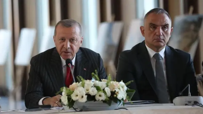 Cumhurbaşkanı Recep Tayyip Erdoğan ve Turizm Bakanı Mehmet Nuri Ersoy bir masada oturuyor, önlerinde çiçek var.