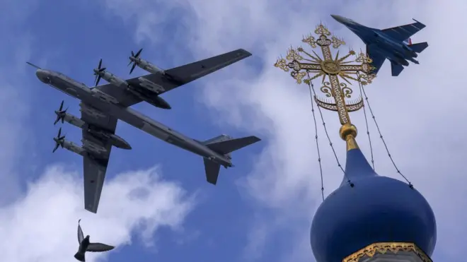 Um avião de combate russo Su-35S e um bombardeiro estratégico Tu-95ms voam em formação sobre uma igreja durante um ensaio para o sobrevoo