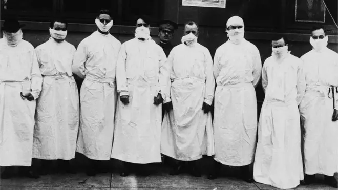Doctors, army officers, and reporters wear surgical gowns and masks while making a tour of a hospital to observe Spanish influenza treatment of patients. -