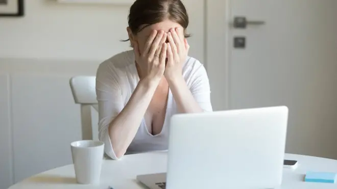 Woman working at desk with laptop, hands closing face