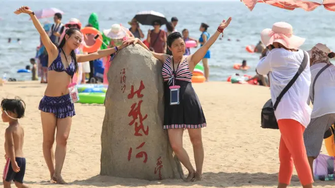 Turistas posando junto a una piedra con inscripciones chinas.