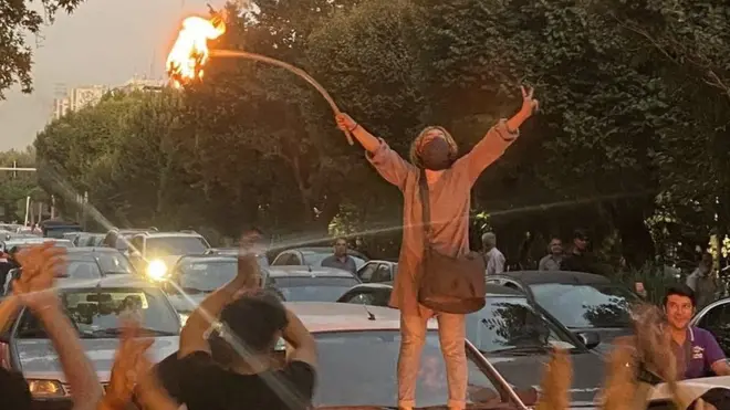 Une femme se tient sur le capot d'une voiture et met le feu à son voile, le 19 septembre 2022, dans le centre de Téhéran, lors des manifestations en faveur de Mahsa Amini.
