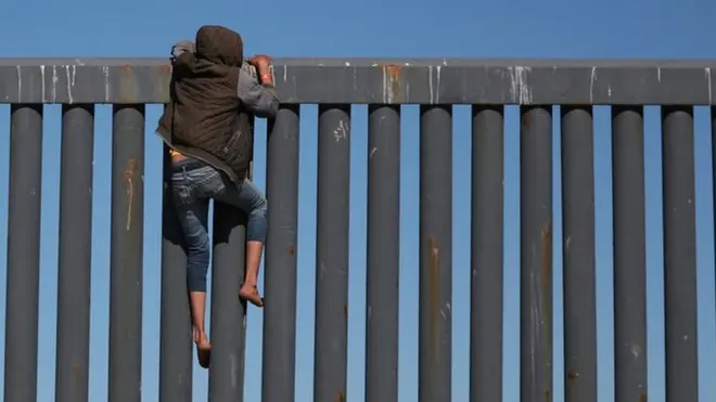 A migrant, part of a caravan of thousands from Central America trying to reach the United States, climbs the border fence