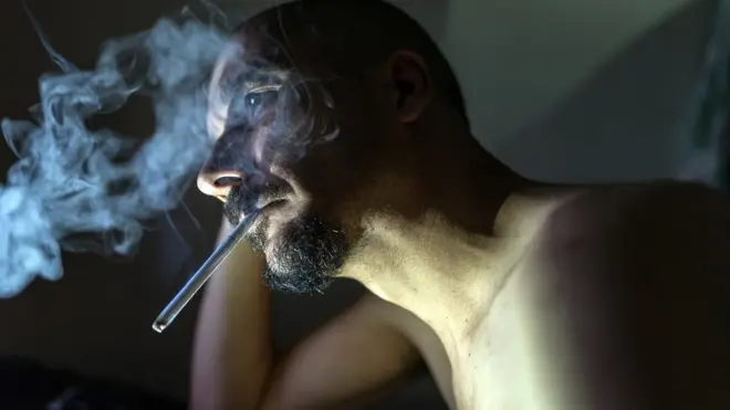 Bearded man smoking, staring vacantly into the distance