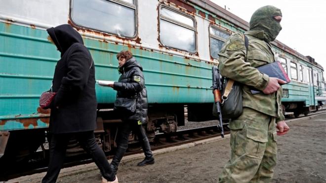 Homem fardado faz guardaaposta ganha aviãozinhofrente a trem, com duas mulheres caminhando atrás
