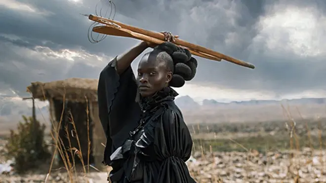 Portrait of a young woman dressed in a Victorian dress and holding traditional Shona cooking utensils