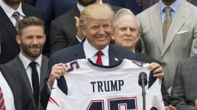 Donald Trump memegang kostum Patriots yang bertulis nama dirinya pada awal tahun ini.