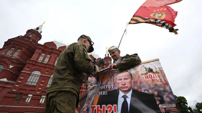 أحد مؤيدي بوتين يحمل صورة كبيرة له في الساحة الحمراء قبل ساعات من الإعلان عن إنتهاء التمرد