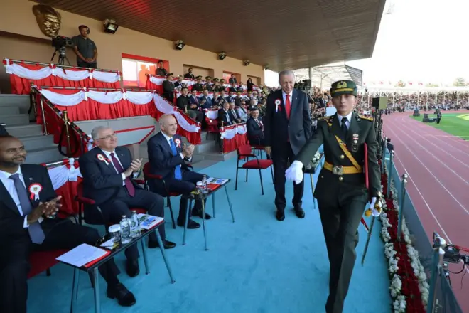 Ebru Eroğlu ve Cumhurbaşkanı Recep Tayyi Erdoğan podyumda. Eroğlu, Erdoğan'ın önünde tören yürüyüşü yapıyor.