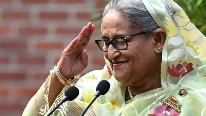 কপালে স্যালুট দেয়ার ভঙ্গিতে হাসছেন ক্ষমতাচ্যুত প্রধানমন্ত্রী শেখ হাসিনা