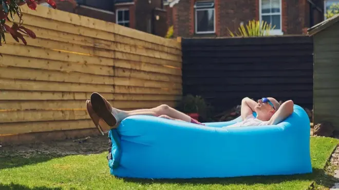 야외 공간 잔디 위 큰 쿠션에 누워 햇빛을 쬐는 남성