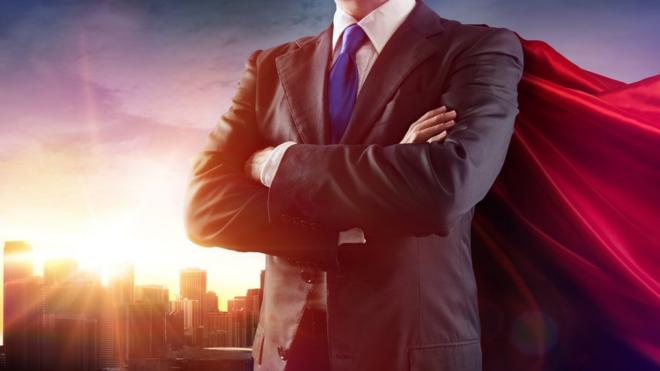Мужчина в деловом костюме и плаще супермена на фоне небоскребов