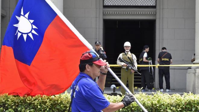 A pro-unification activist displays a Republic of China flag near the roped-off rear entrance to the Presidential Palace complex, where a samurai sword-wielding attacker slashed a police guard, in Taipei on August 18, 2017.
