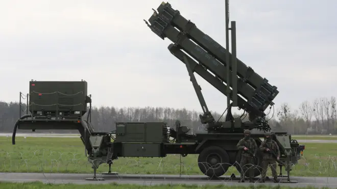 Two armed people in camouflage stand in front of a Patriot missile system