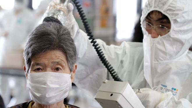 Trabajadora midiendo la radioactividad en una mujer luego del accidente en la planta nuclear en Fukushima