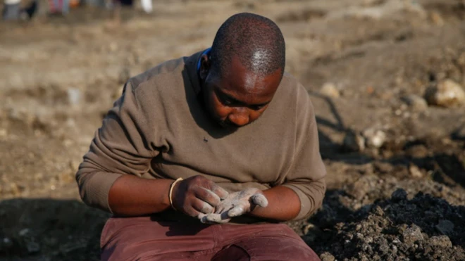 Seorang pria memeriksa pasir di tangannya, mencari berlian.