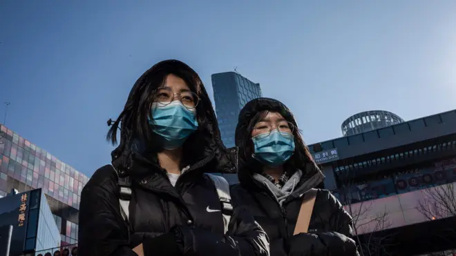 People wear protective masks as they walk outside a shopping mall in Beijing on January 23
