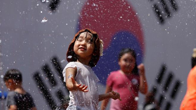 A South Korean girl is splashed with water as she stands in front of her country's flag.