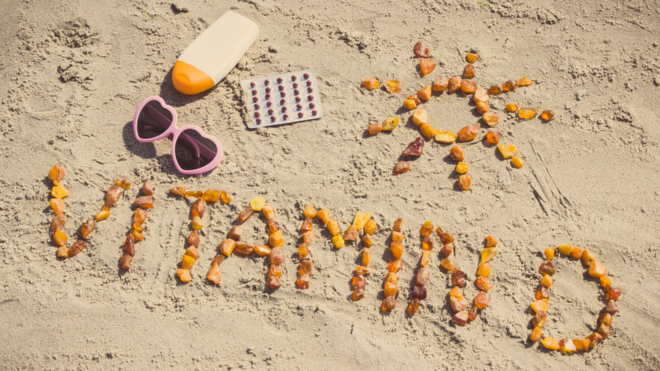'Vitamina D' escrito com conchas e pedras na areia da praia