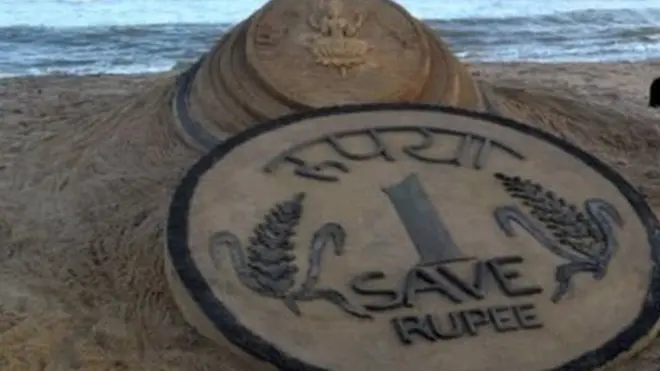 रेत पर बनी रुपये की प्रतिकृति