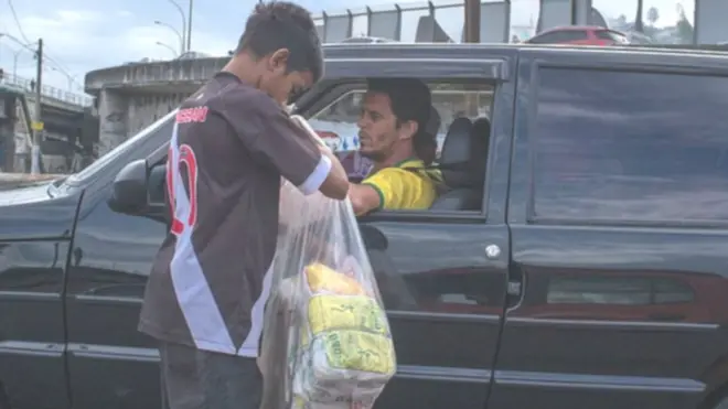 Menino vendendo biscoitof12 bet jogo do foguetepolvilho para motorista parado no trânsito