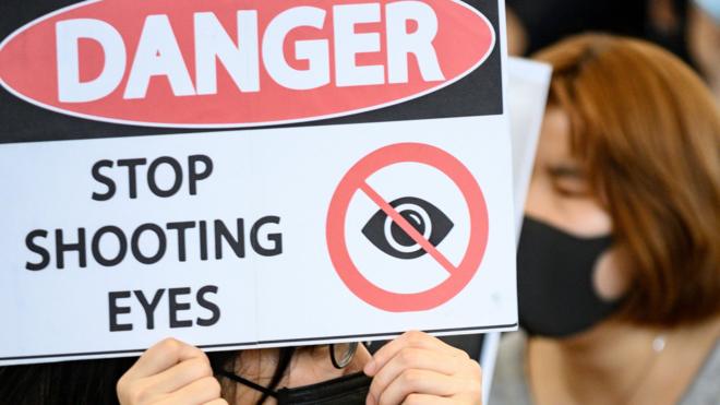 香港国际机场一号客运大楼内一名女示威者举起“危险，停止射击眼睛”标语（13/8/2019）