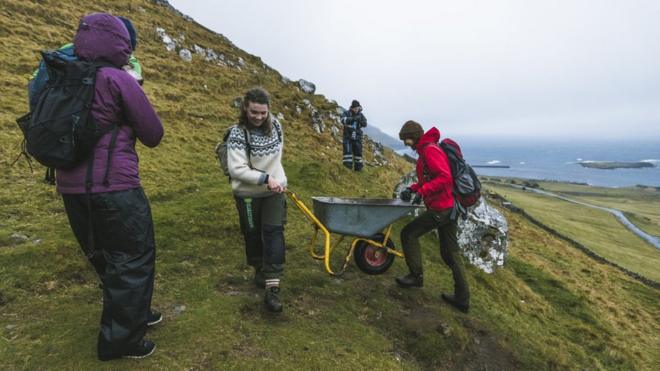 Brown Group members help each other to push a wheelbarrow in the hills in Kirkjubøur