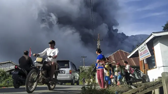 Sejumlah pengendara melintas di Jalan Karo-Langkat dengan latar belakang Gunung Sinabung yang menyemburkan material vulkanik di Desa Kutarayat, Naman Teran, Karo, Sumatera Utara, Kamis (13/8). Pusat Vulkanologi dan Mitigasi Bencana Geologi (PVMBG) menyatakan Gunung Sinabung berstatus level III atau siaga dan meminta masyarakat untuk tidak melakukan aktivitas di desa yang telah direlokasi.