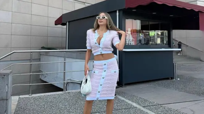 Pembe twid bir takım giyen bir kadın elinde çantasıyla İstanbul Adliyesi merdivenlerinde duruyor, güneş gözlükleri takmış. 