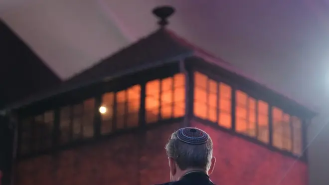 Seorang pria memakai kippah berdiri di dekat menara utama bekas kamp konsentrasi Auschwitz.