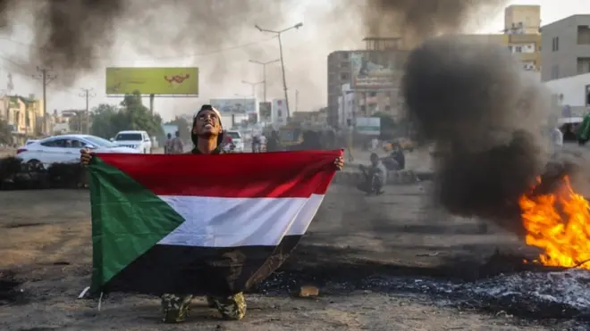 شاب سوداني يحلم علم السودان ويتطلع إلى السماء