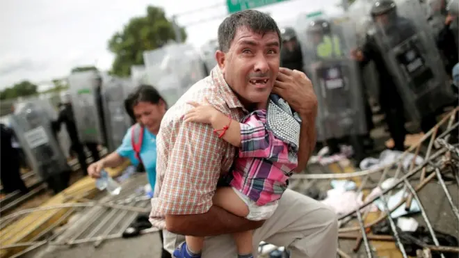 Un migrante hondureño protege a su hijo después de que otros miembros de la caravana derribaran una valla fronteriza en el lado guatemalteco.