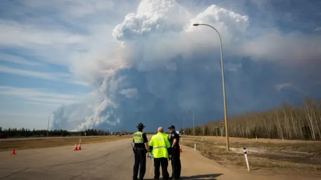 Police officers look as smoke billows from a wildfire in Fort McMurray, Canada. Photo: 4 May 2016