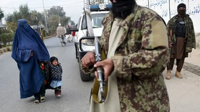 Mulher e criança passam por membros do Talebã em Jalalabad, perto da fronteira com o Paquistão, em foto recente; grupo retomou o poder em agosto