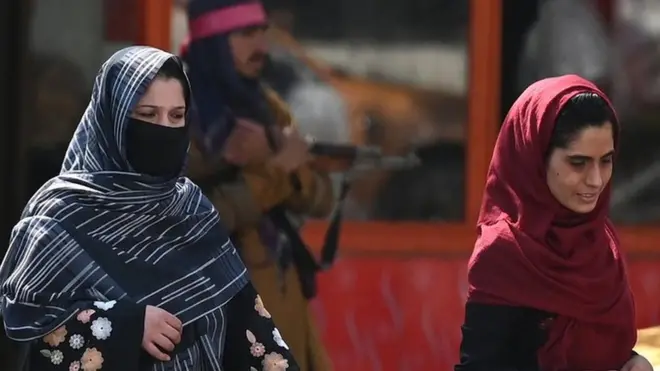 Afghan women walk past a Taliban fighter in a Kabul street