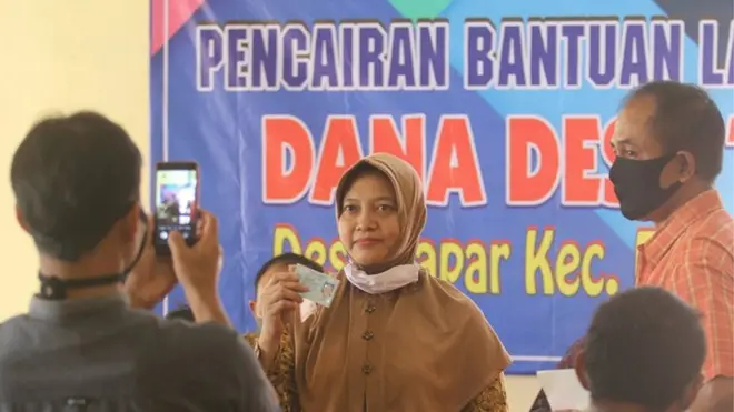 Seorang warga terdampak pandemi Covid-19 memperlihatkan uangnya kepada petugas untuk difoto sebagai tanda bukti saat pengambilan bantuan sosial (bansos) Dana Desa di Desa Papar, Kediri, Jawa Timur, Mei lalu.