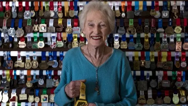 Deirdre Larkin stands in front of a wall with her medals on it.