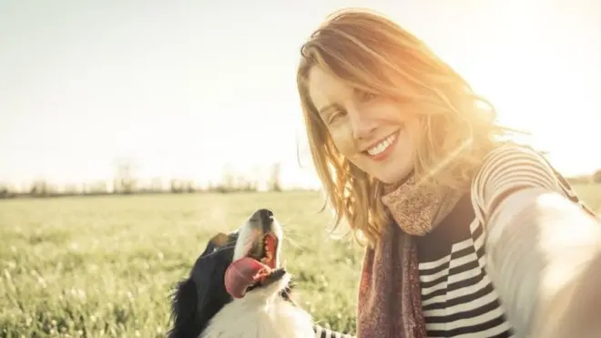 فتاة تنظر مبتسمة إلى الكاميرا وهي تلتقط صورة سيلفي مع كلبها