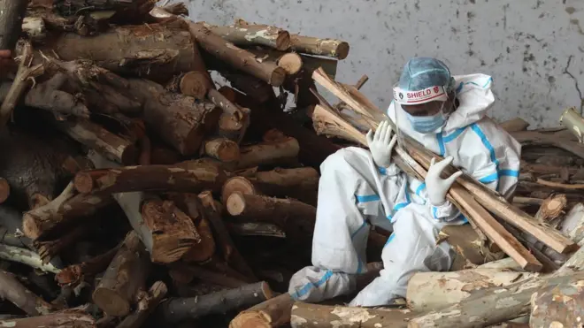 Image shows a relative of a Covid victim holding kindling for use in funeral pyres