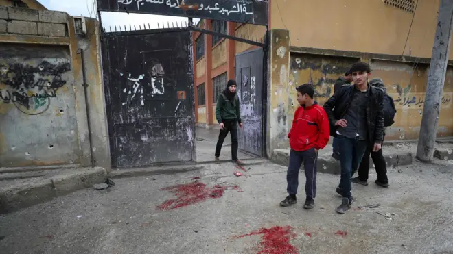 People stand next to patches of blood outside a school in the opposition-held town of Sarmin, Syria, that was reportedly hit by cluster munitions fired by government forces (1 January 2020)