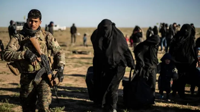 أحد مقاتلي قوات سوريا الديمقراطية يشرف على خروج نساء وأطفال من الباغوز