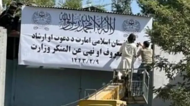 People on a mechanical crane attend to a white signboard outside a building in Kabul