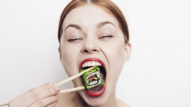 Mulher abrindo a boca para comer sushi,aposta para jogo do brasilolhos fechados