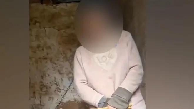 Скріншот з відео, на якому видно жінку в халупі, яка прикута ланцюгом за шию