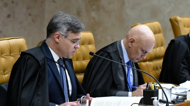 Mendonça lê voto durante julgamento no STF, enquanto Moraes vê seu celular, curvado, olhando para baixo