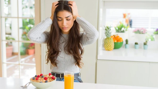 Portakal suyu ve mısır gevreğine bakarak başını tutan bir kadın