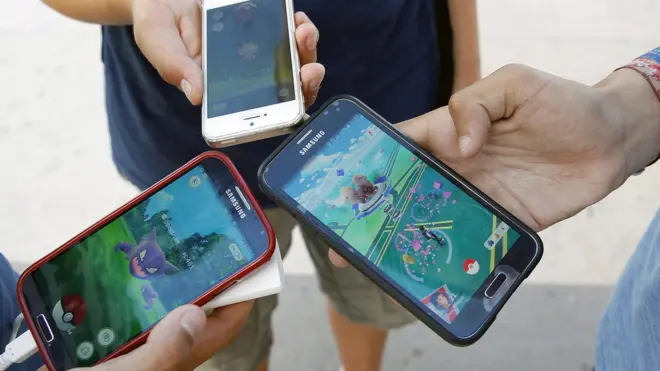 Três pessoas seguram celulares com tela mostrando o game do Pokémon Go