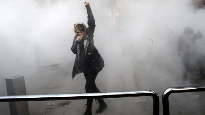 An Iranian woman raises her fist amid the smoke of tear gas